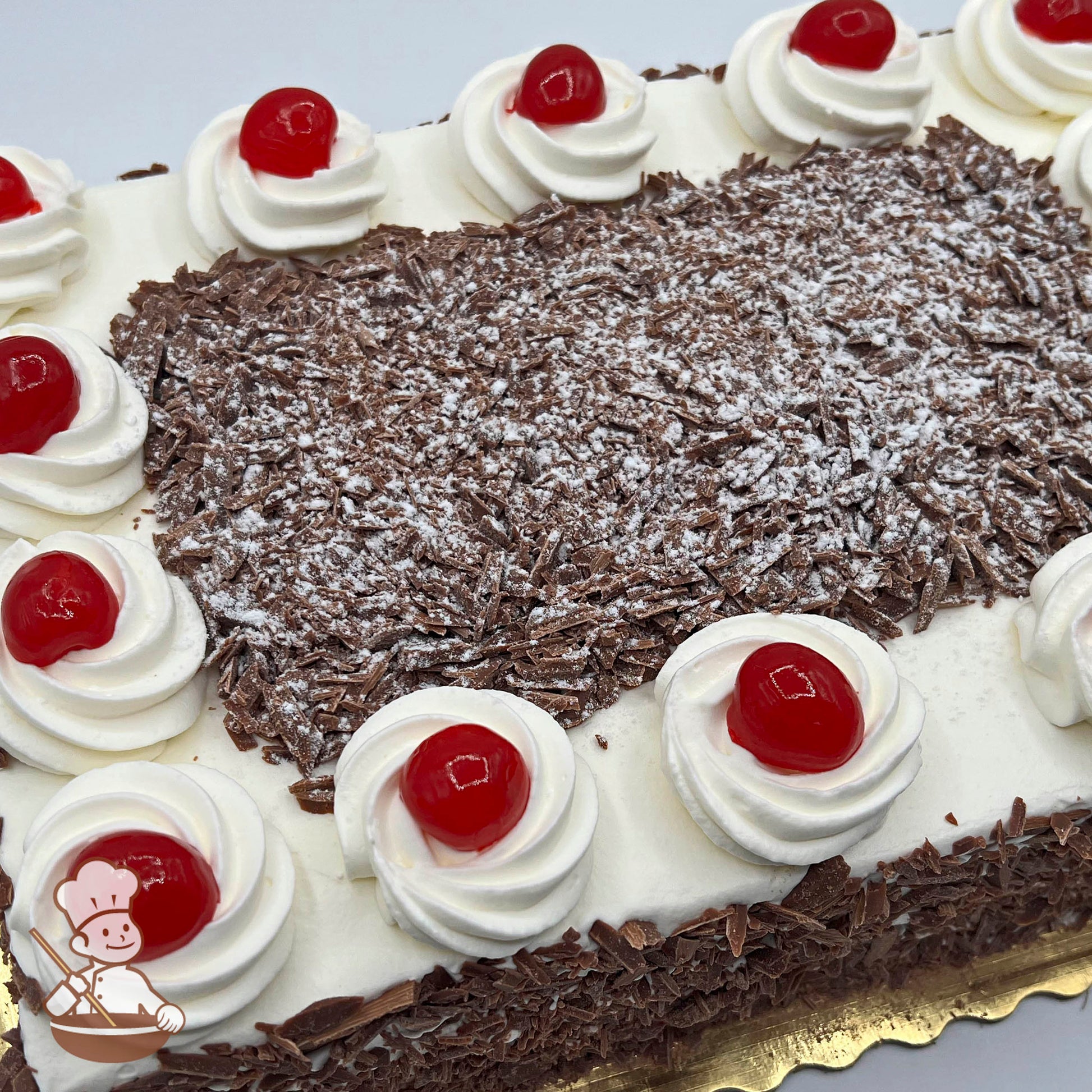 Sheet cake with whipped cream swirls topped with cherry preserve and surrounded by chocolate shavings.