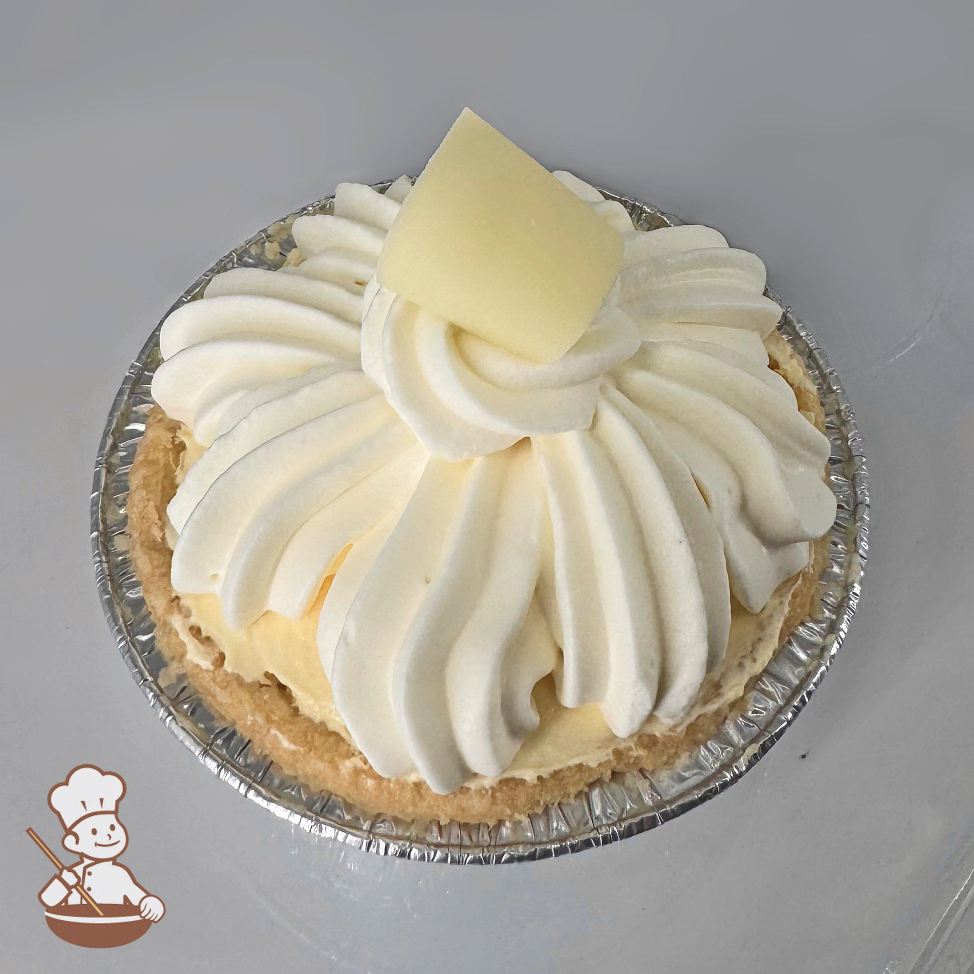 Mini banana cream pie topped with swirls of whipped cream and a white chocolate curl, in a foil pie tin.