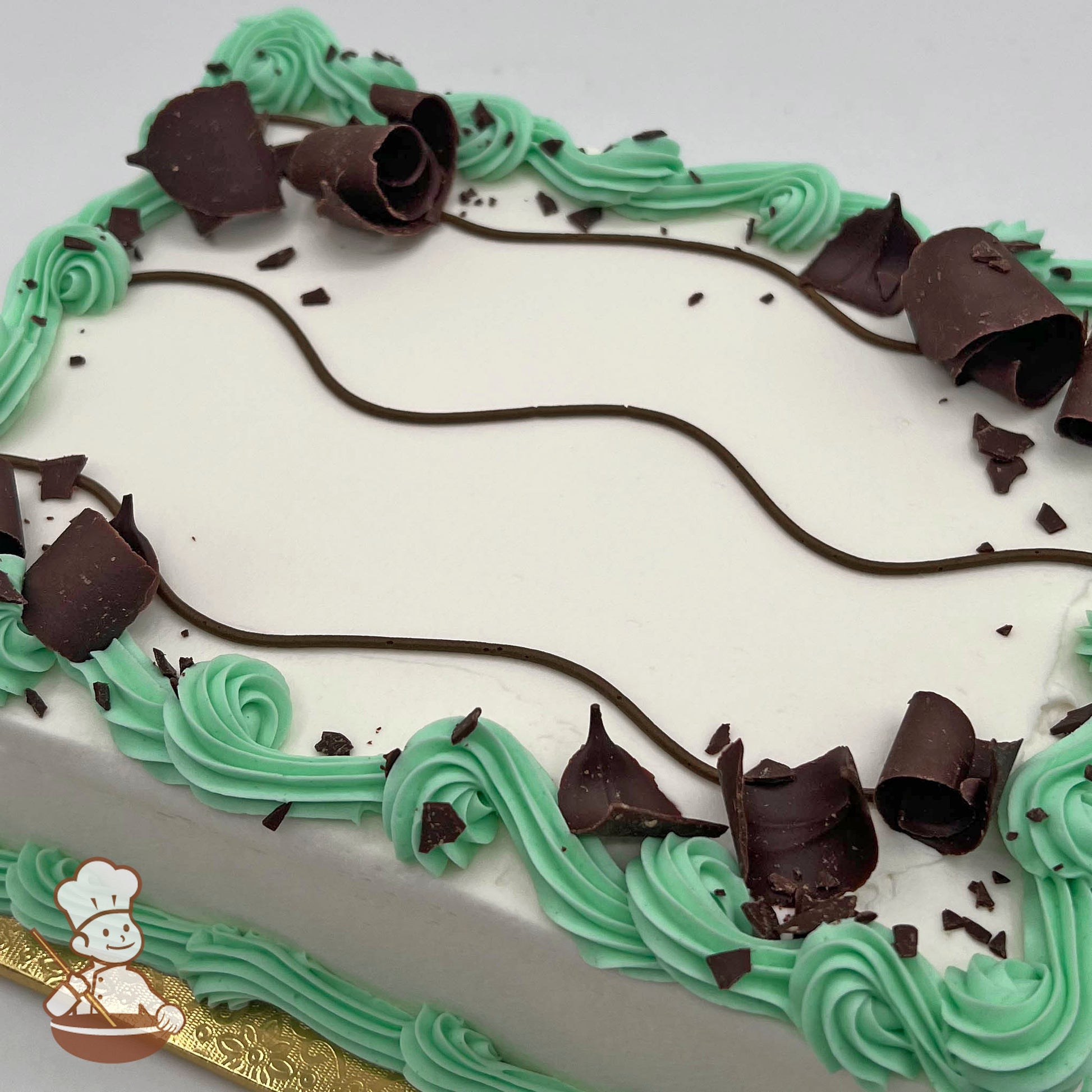 Rectangular cake with white frosting, decorated with mint green swirls and chocolate curls. Chocolate lines crisscross the top.