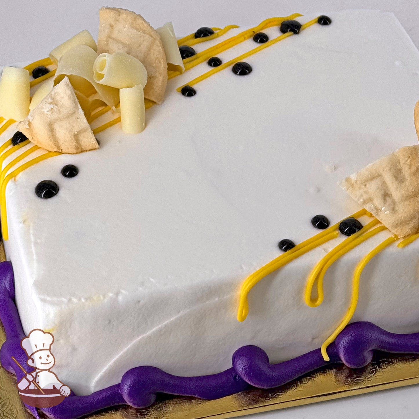 Rectangular white cake with passion fruit mousse filling, topped with buttercream icing, yellow drizzle, black dots, and cookie pieces. Purple icing border.