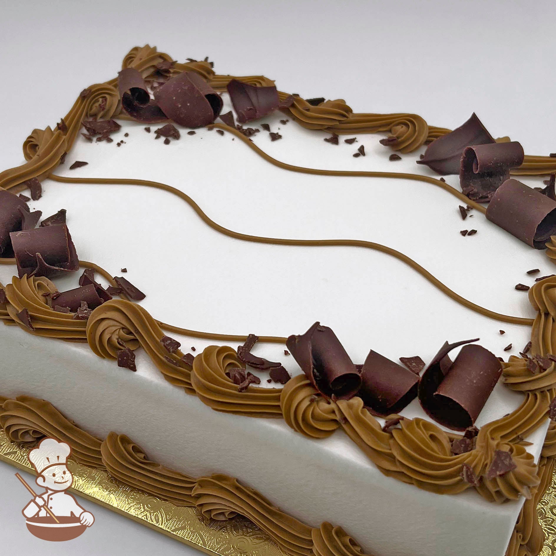 Rectangular cake with smooth white buttercream icing, decorated with brown swirls and chocolate curls. 