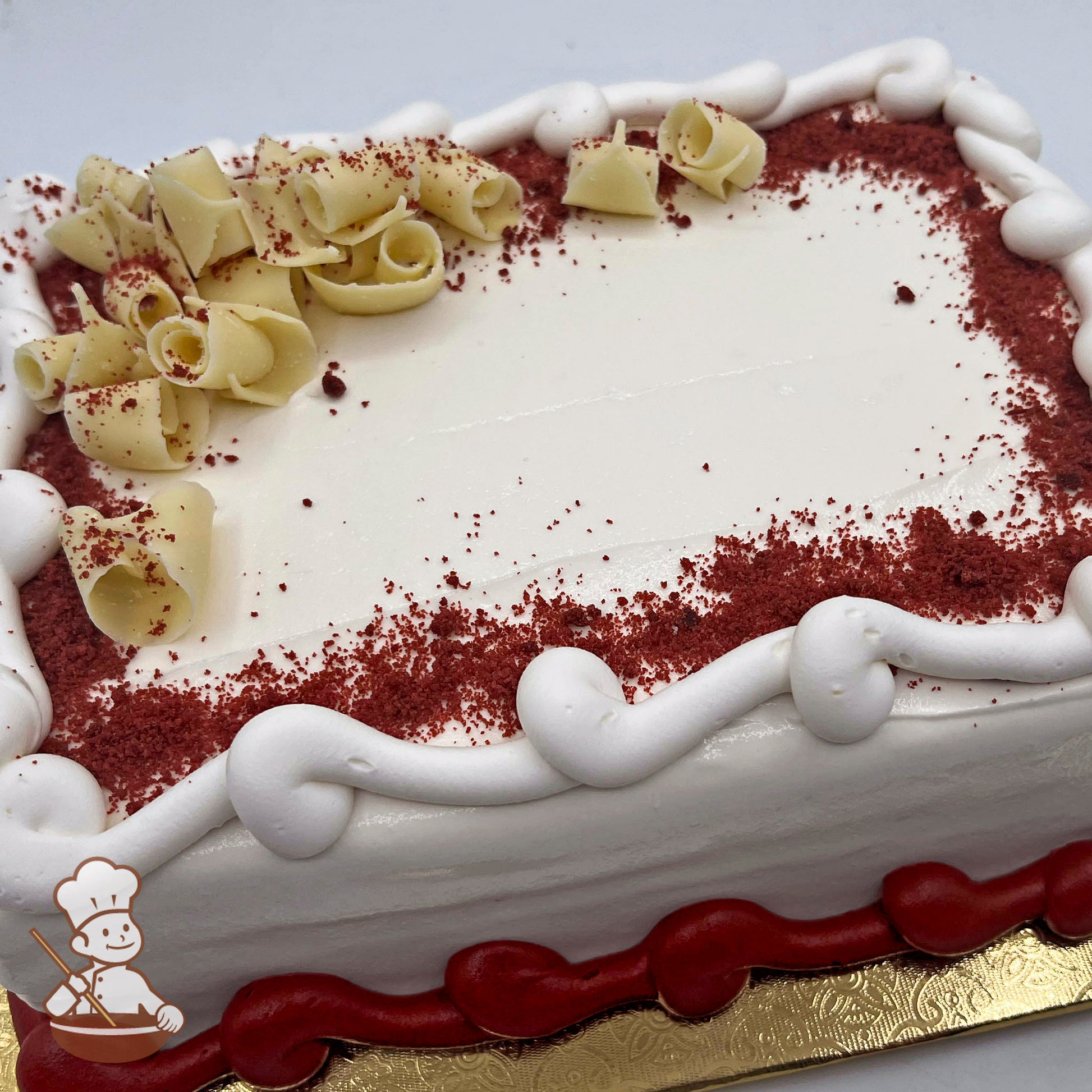 Red velvet sheet cake with white icing, white and red piped borders, white chocolate curls, and red velvet crumbs.