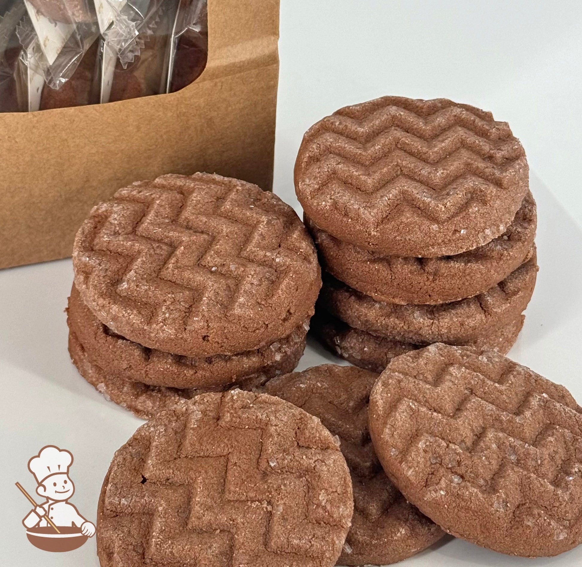 Ten chocolate shortbread cookies with a light, airy texture and topped with sugar crystals are stacked in front of a kraft window bag.