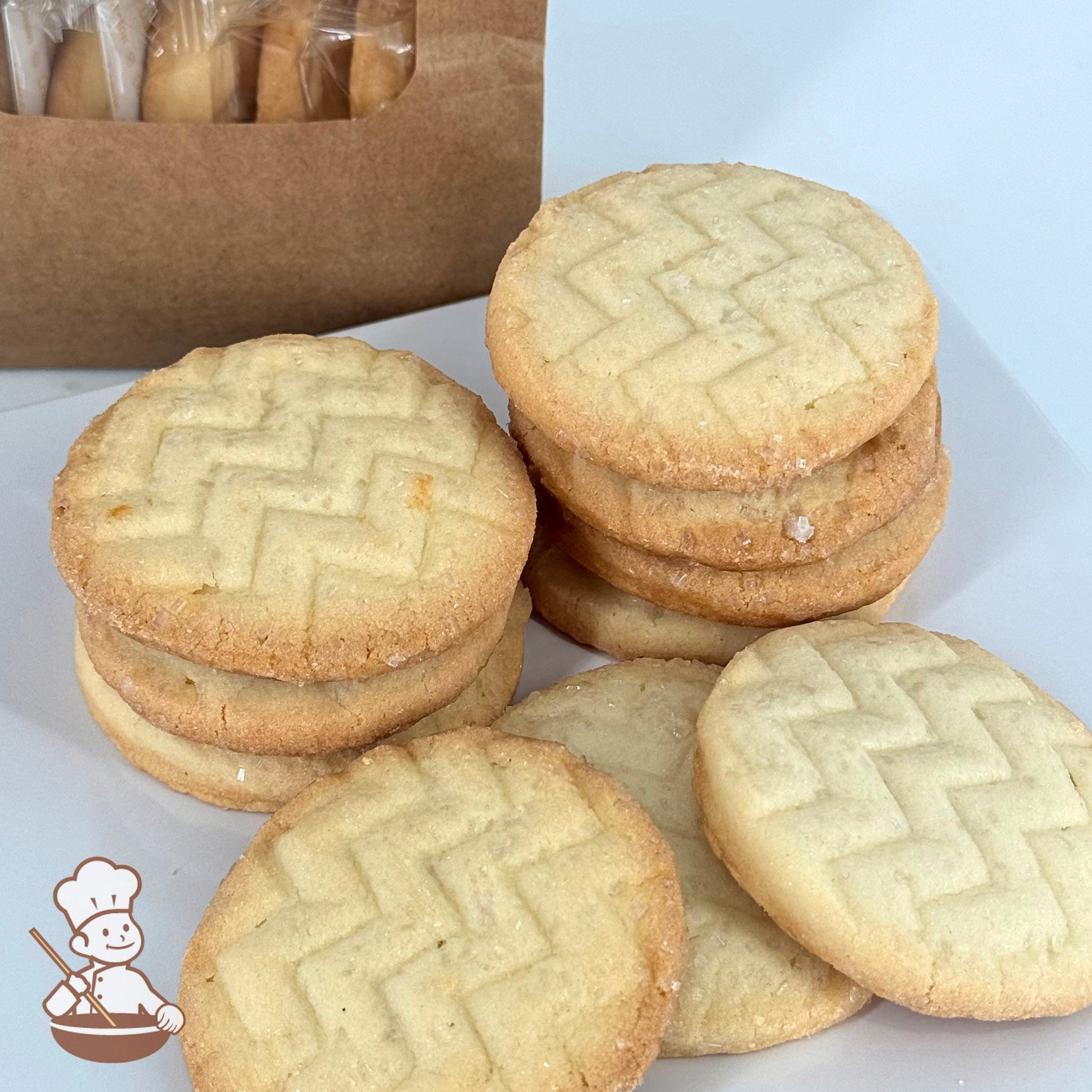 Ten lemon-flavored shortbread cookies with a light, airy texture and topped with sugar crystals are stacked in front of a kraft window bag.