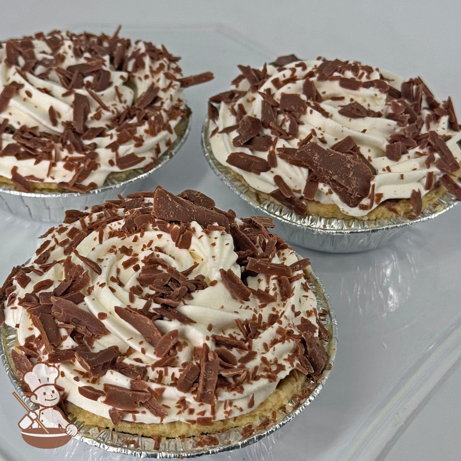 Three mini pies in foil tins with chocolate cream filling, topped with whipped cream and Belgian chocolate shavings.