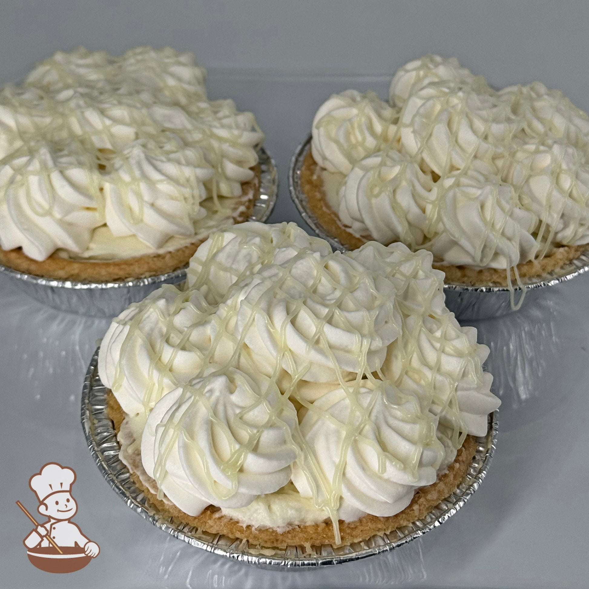 Three mini key lime cream pies in foil tins with whipped cream topping and key lime curd drizzle.