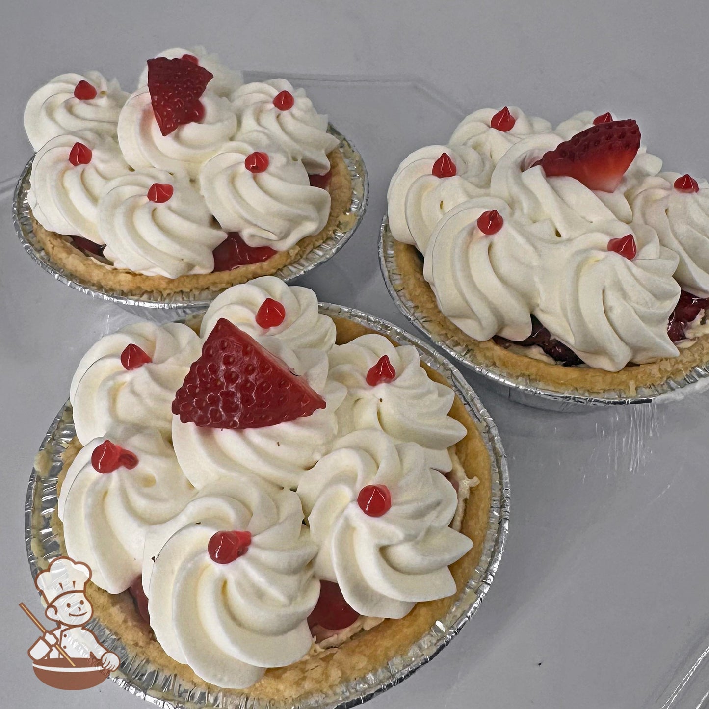 Three mini pies in foil tins with Bavarian cream filling, whipped cream topping, and strawberry glaze dots, each garnished with a slice of strawberry.