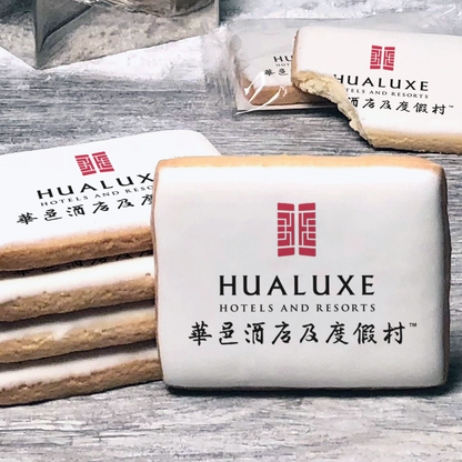 A stack of rectangle butter shortbread cookies with Hualuxe logo printed directly on a white, lemon sugar icing.