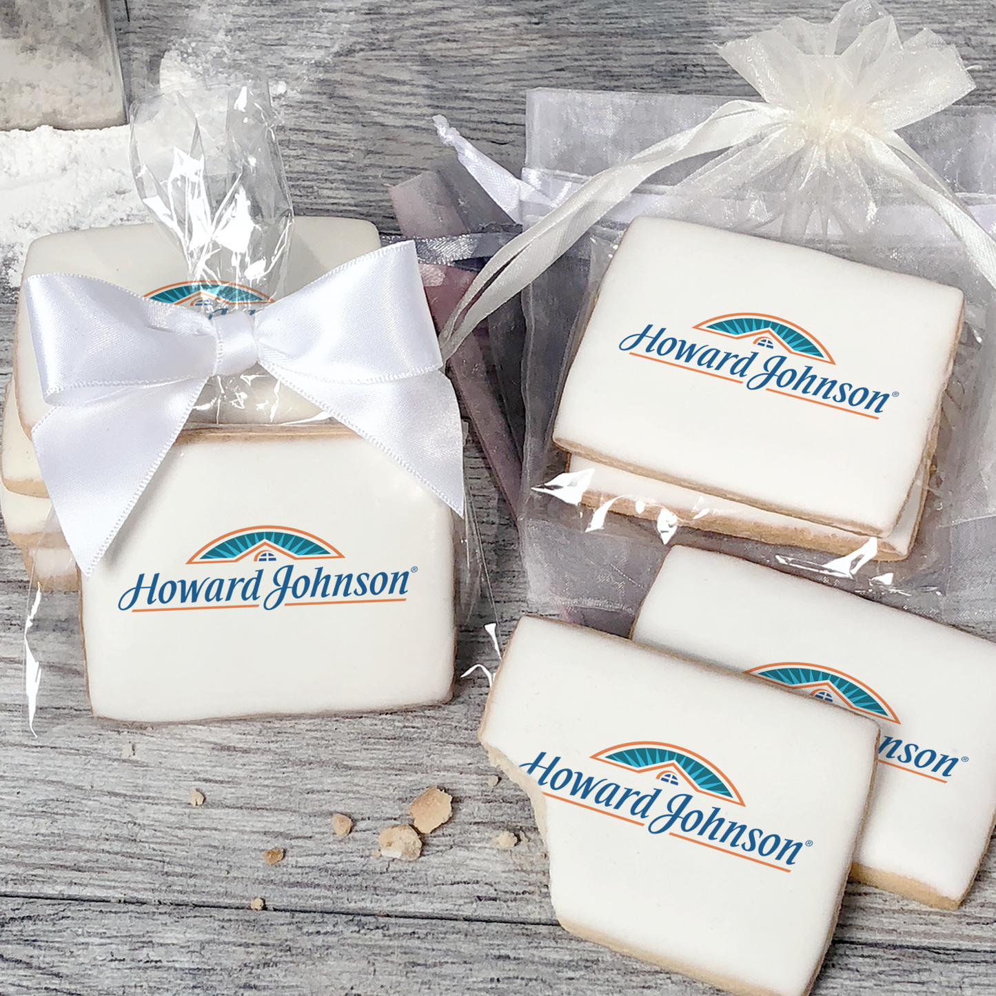 A stack of rectangular butter shortbread cookies with Howard Johnson logo printed directly on a white, light sugar icing. Some cookies are shown in clear packaging with a twist-tie ribbon bow or inside an organza bag.