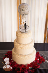 3 tier ivory fondant cake with cream color vintage piping and red rose petals on base.  Hot air baloon topper finishes the cake.