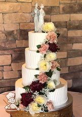 4-tier cake with white icing and decorated with a vertical curve stripe texture and white buttercream beaded trims.