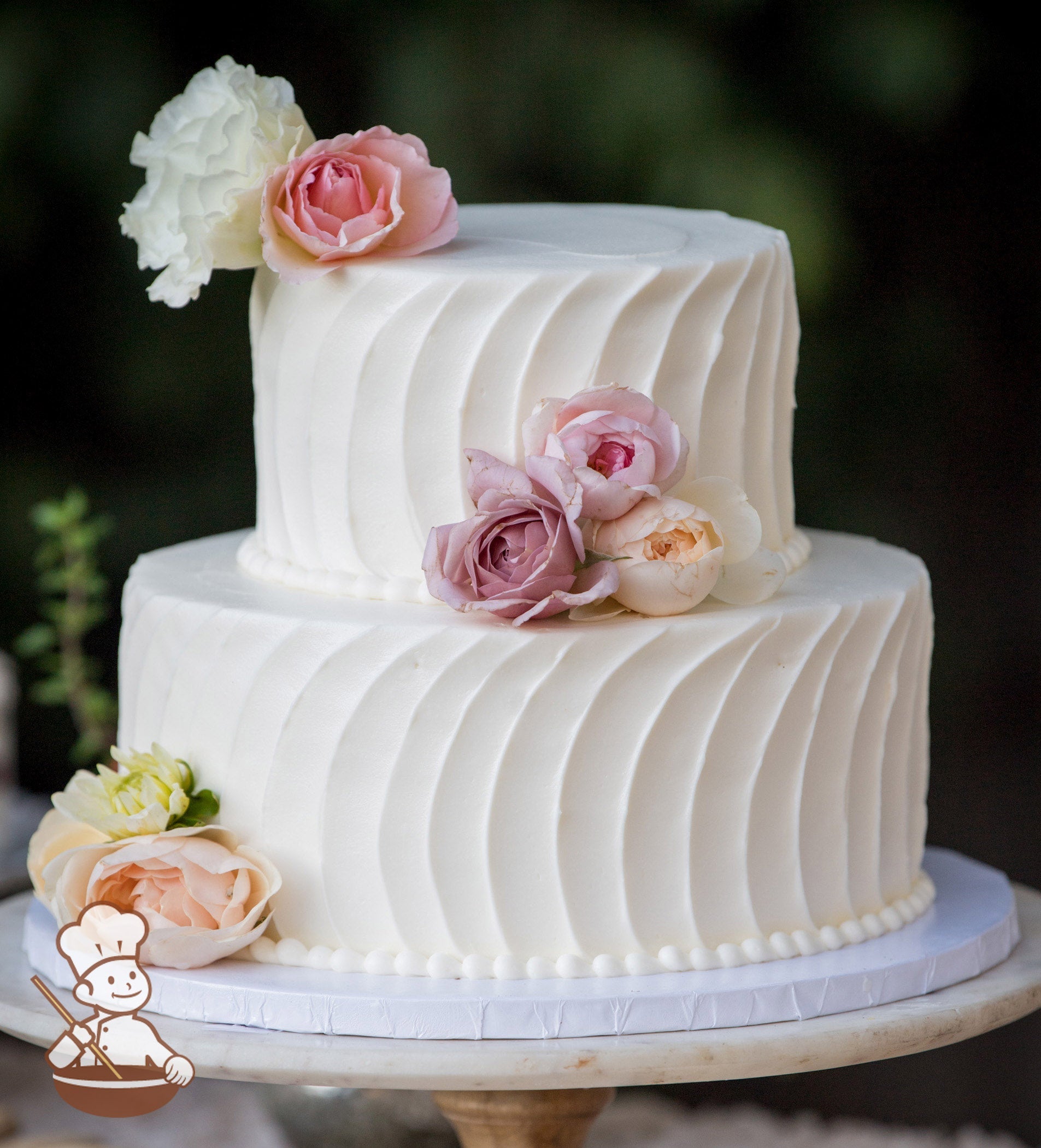 2-tier cake with white icing and decorated with a vertical curve stripe texture and white buttercream beaded trims.