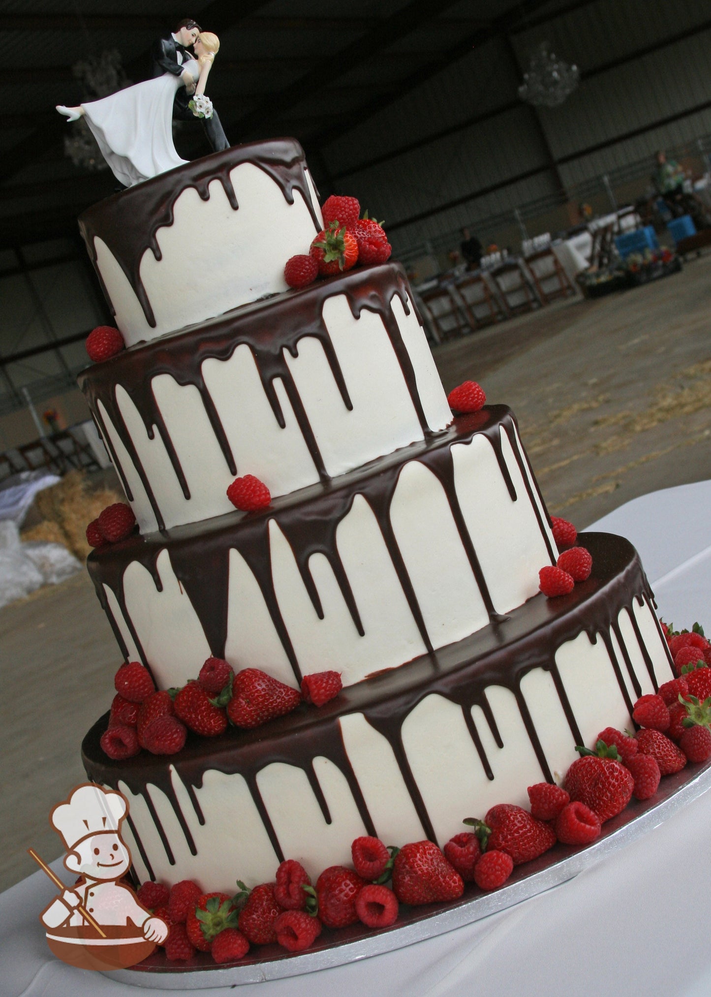 4-tier cake with smooth white icing and decorated with a chocolate ganache pour and fresh strawberries and raspberries.