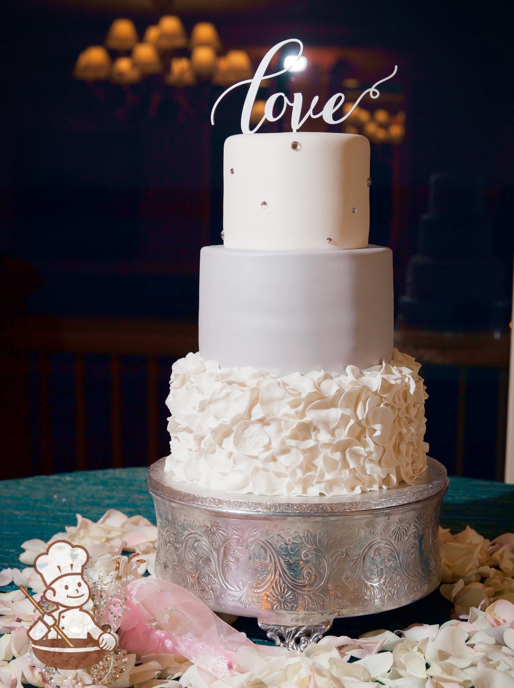 3 tier fondant wedding cake with fondant flower petal ruffle bottom tier, smooth gray middle and white top tier finished with rhinestone beads.