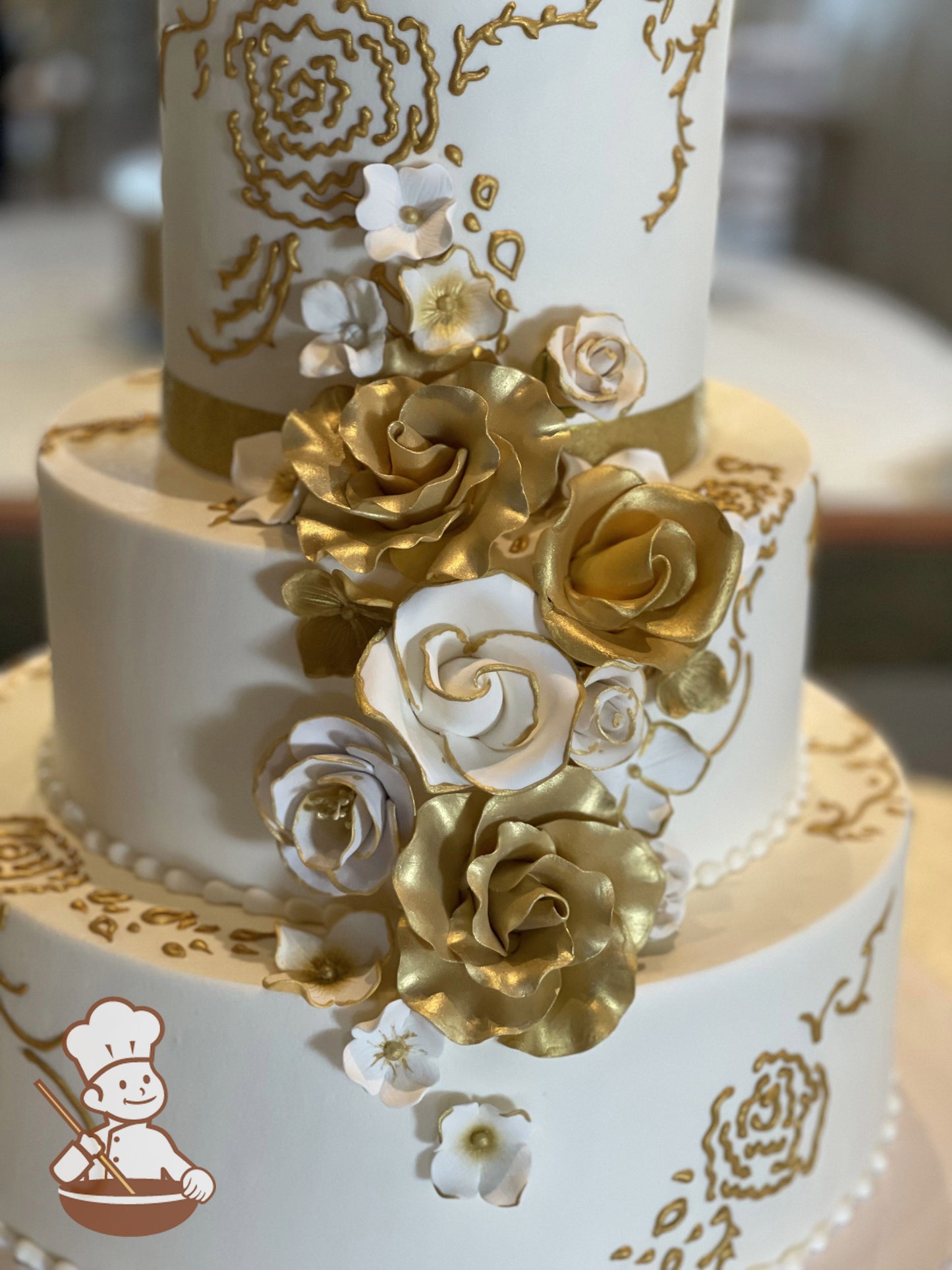 3-tier white cake with hand-piped gold accents and white sugar flowers with added gold coloring.