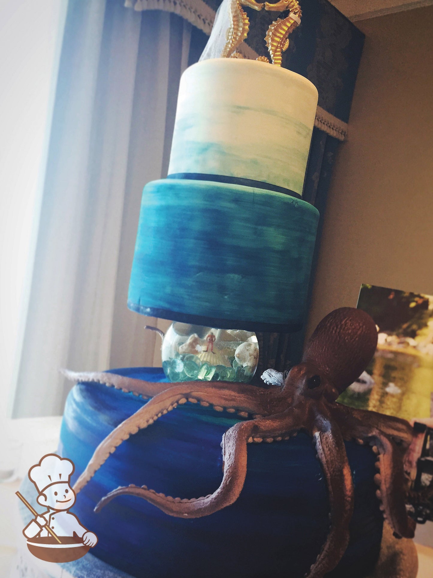 3-tier cake cake decorated with blue ombre scraped coloring to look like the ocean and a pillar on top of the bottom tier with a big octopus.