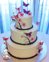 3-tier cake with cherry blossom branches in green and pink. Pink and purple butterflies decorated coming out of the cake.