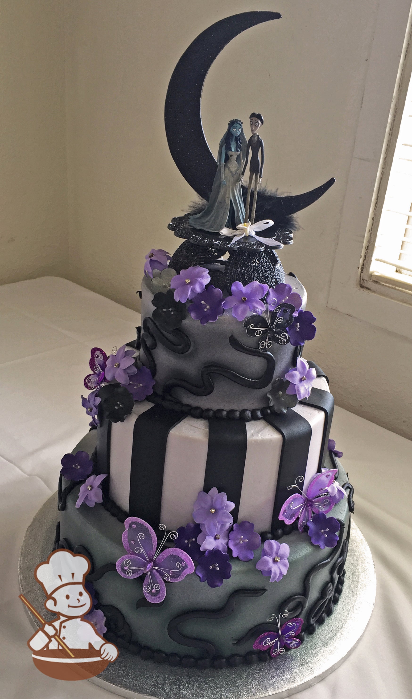 3-tier cake with sprayed light black and black piping. Middle tier with black and white stripes. Decorated with purple flowers and butterflies.